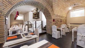 A dining area with brick arches, white chairs, and tables set for a meal. - Hotel Metropolis (Rome)