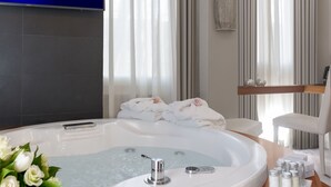 A modern bathroom with a large bathtub, a wooden vanity, a flat-screen TV, and neatly folded towels. - Hotel Metropolis (Rome)