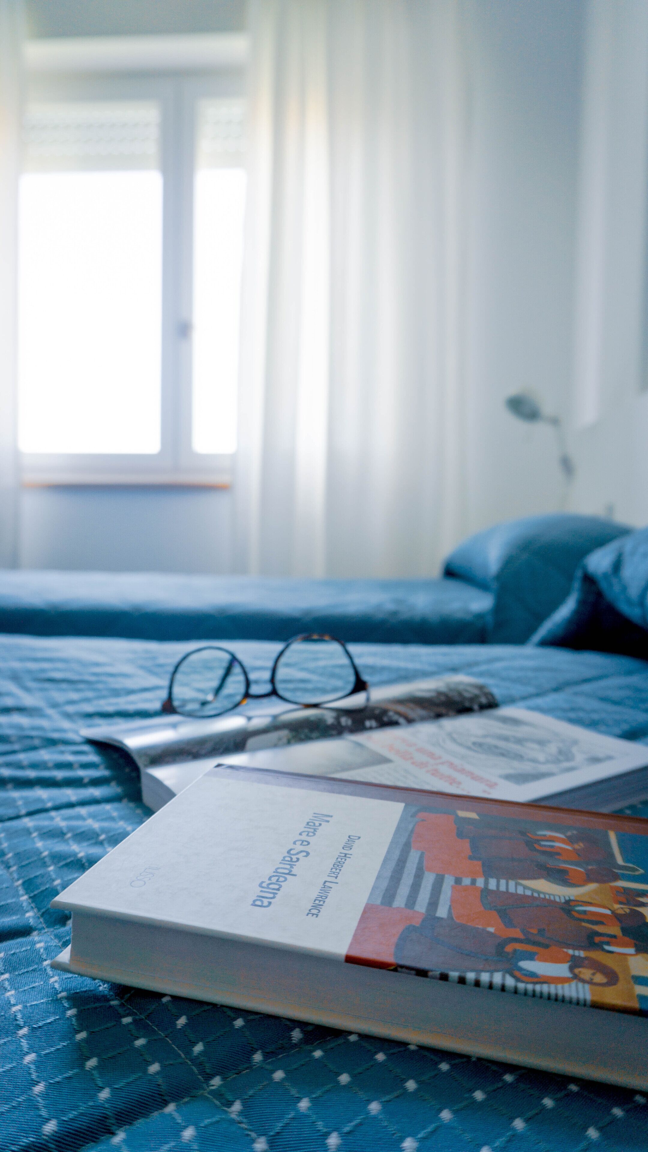 Una cama con una manta azul, un par de gafas y un libro sobre una mesa.