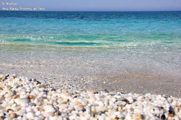 A pebbled beach with clear turquoise water. - Mistral Hotel (Oristano)