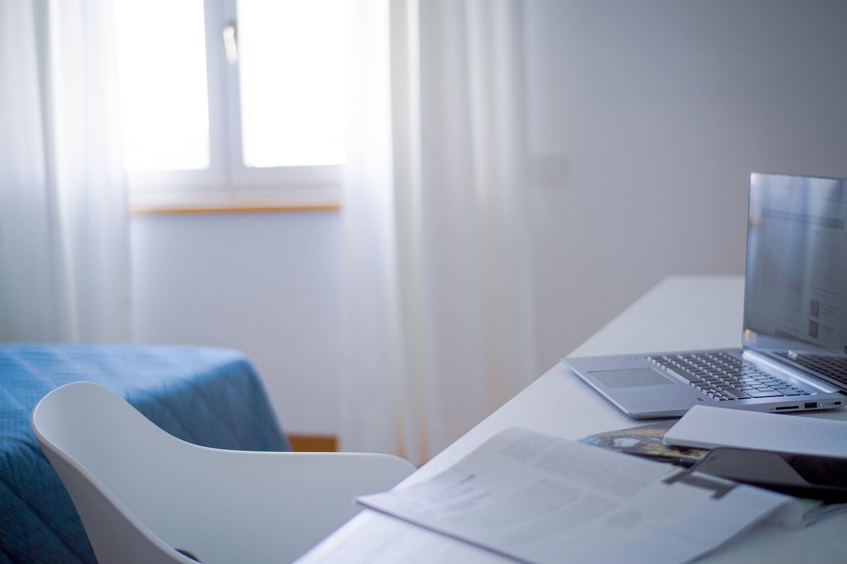 A hotel room with a desk, laptop, and paperwork.