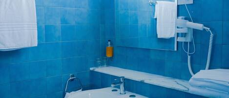 A bathroom with blue tiles, a white sink, a toilet, and a window above the mirror.