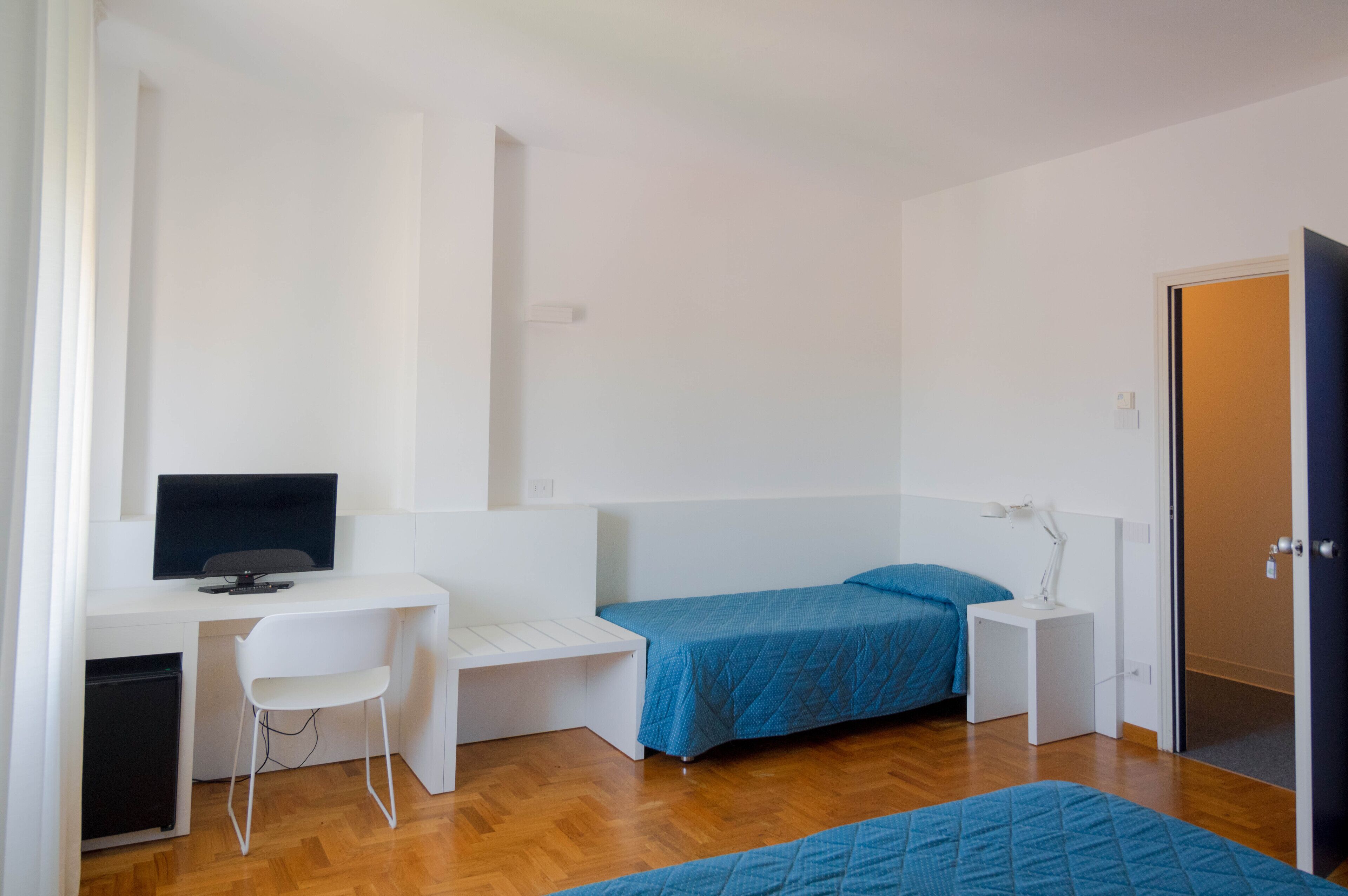 A bedroom with a bed, a desk, a chair, and a television.