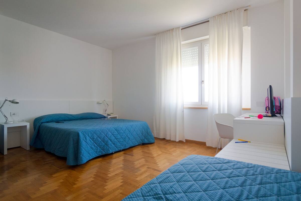 A bedroom with a bed, a desk, a chair, and a window with curtains.