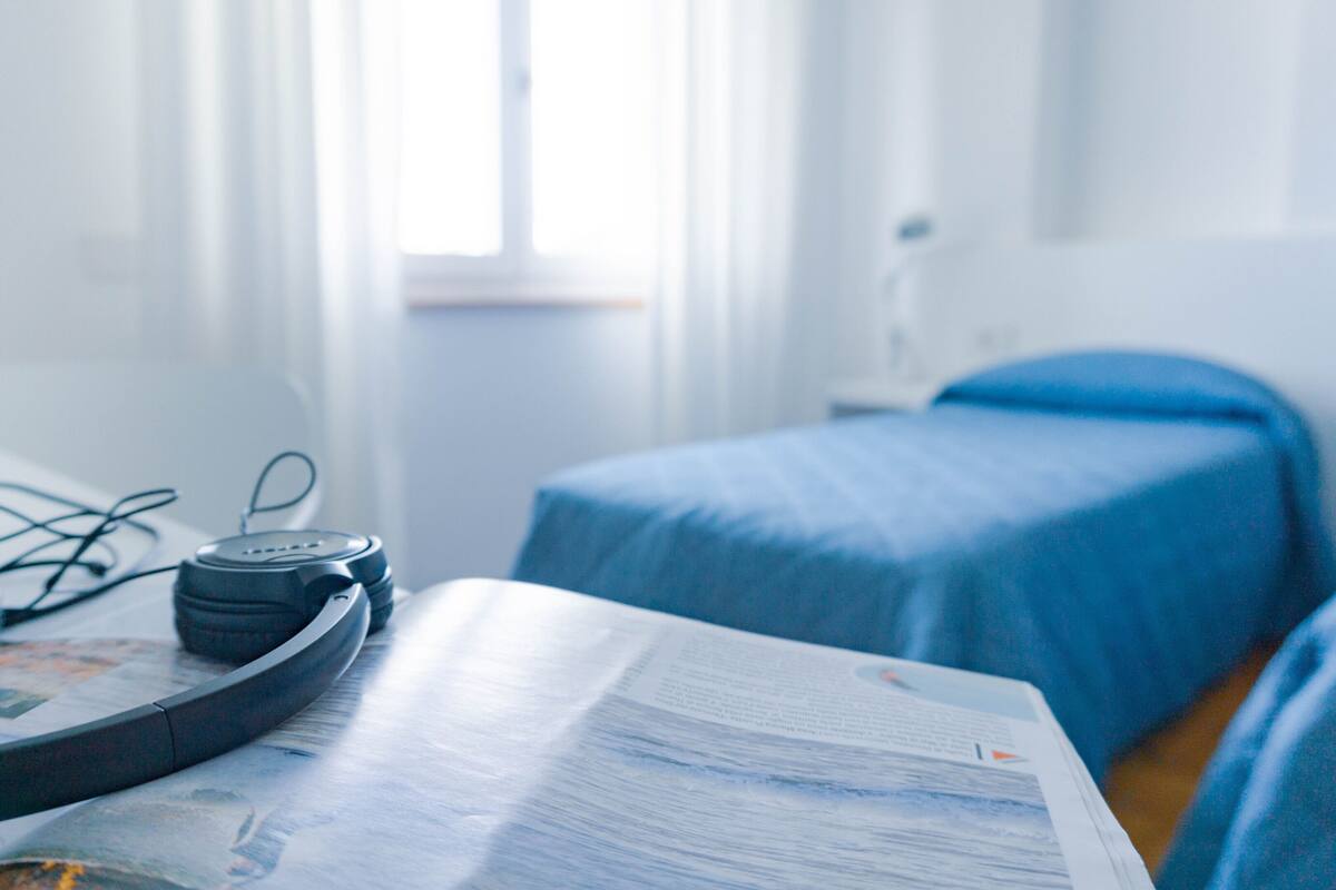A hotel room with a bed, a bedside table with a book, and a pair of headphones on the table.