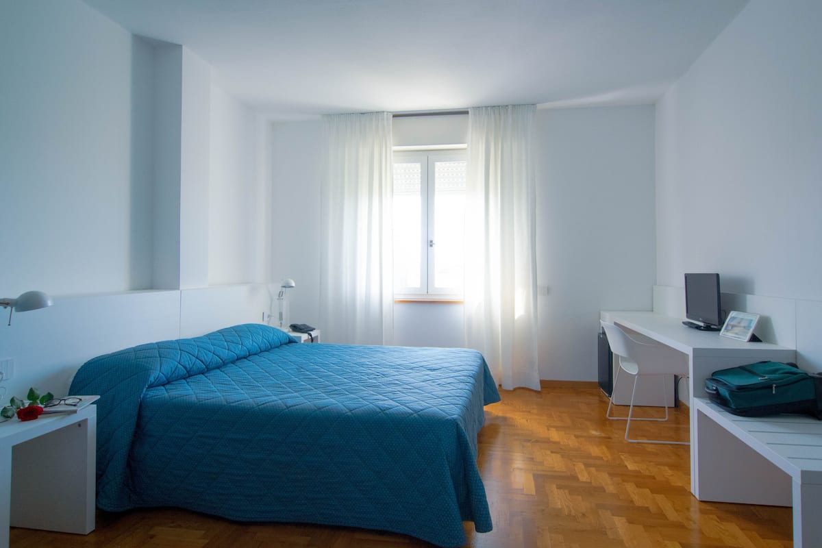 A bedroom with a bed, a desk, a chair, and a window with curtains.