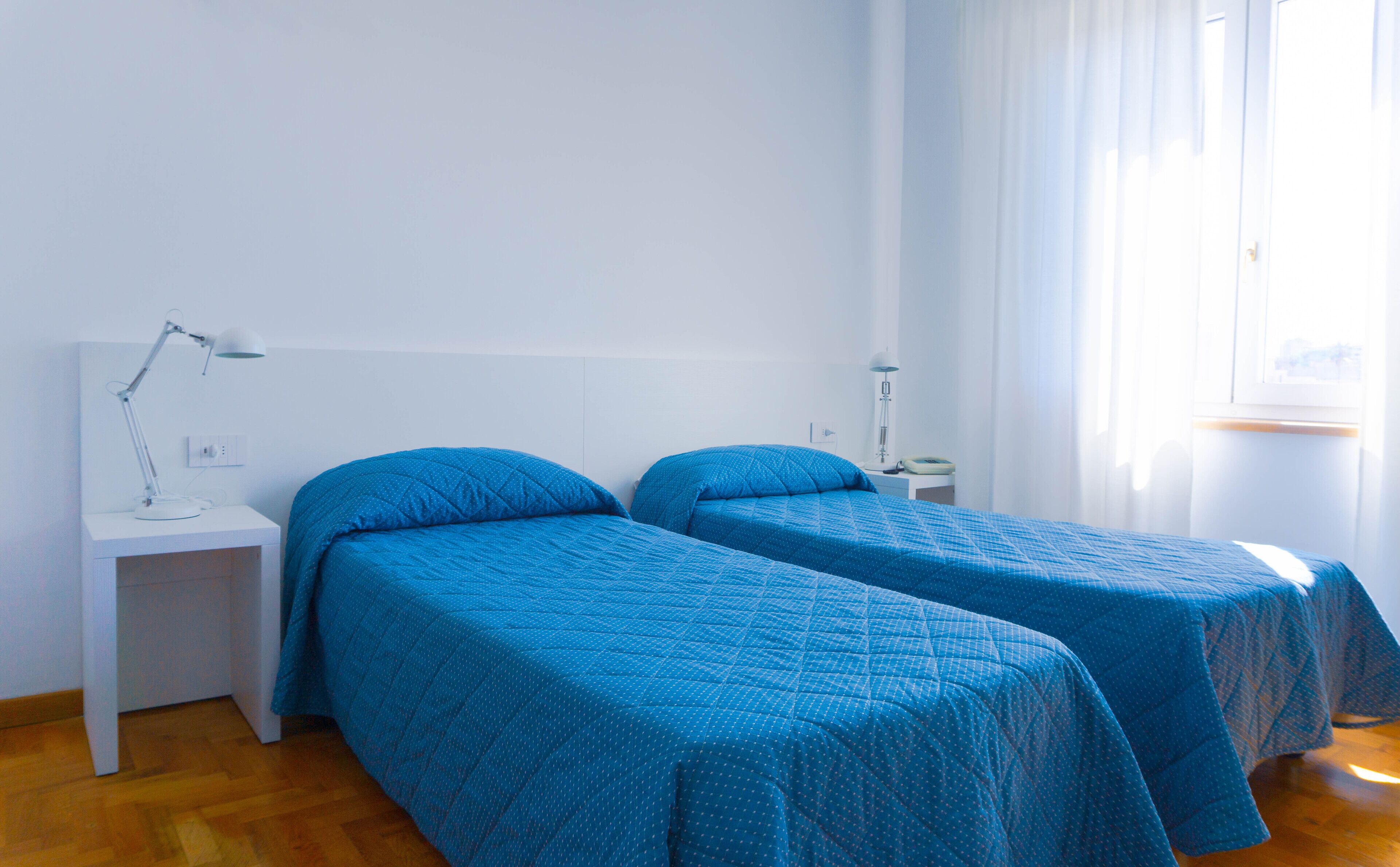 Une chambre avec deux lits simples, une table de chevet avec une lampe, une commode et une fenêtre avec des rideaux.