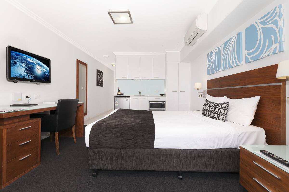 A hotel room with a bed, desk, chair, and kitchenette.