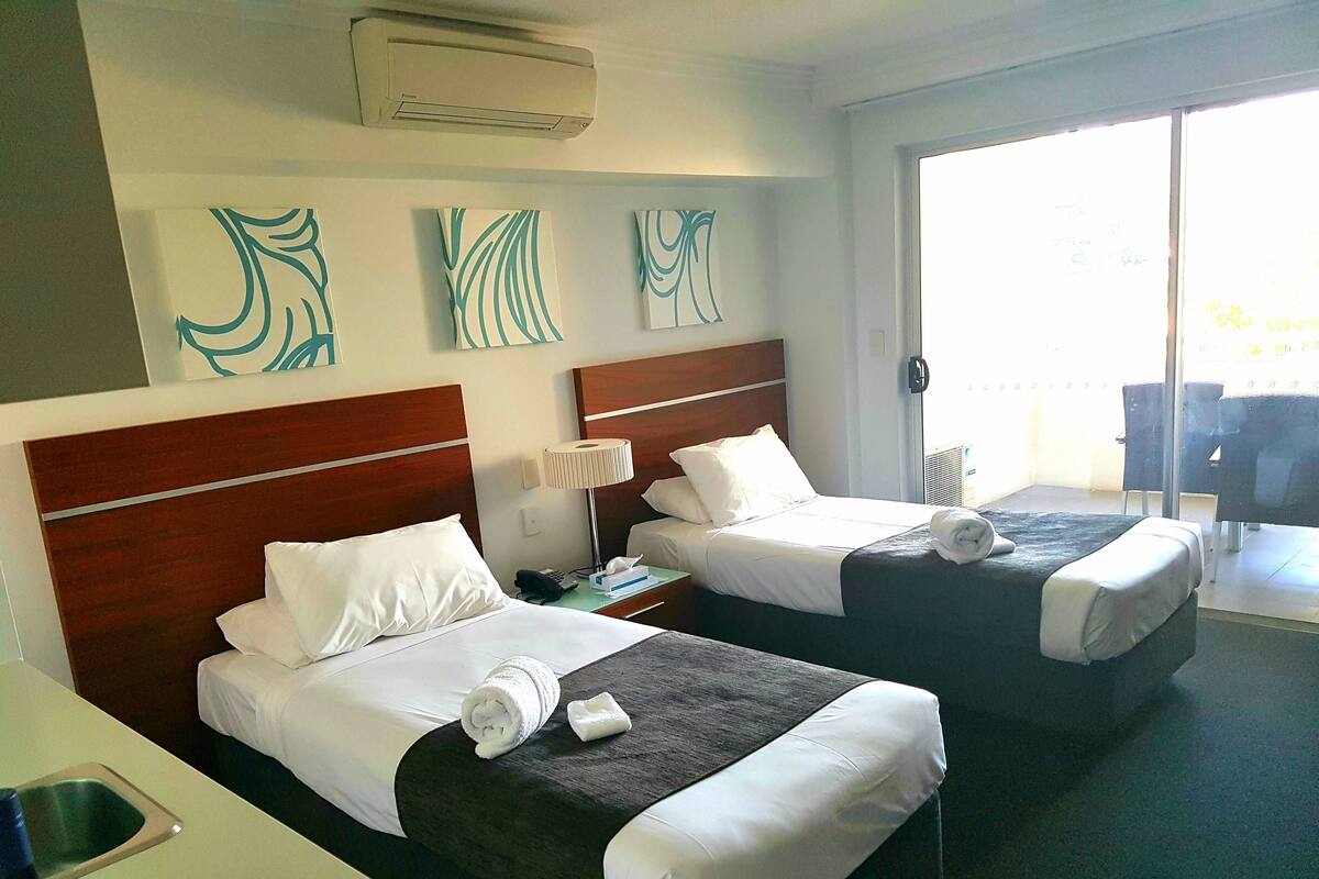 A hotel room with two beds, a minibar, and a view of the outdoors.