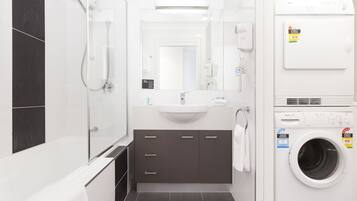 Un baño moderno con bañera, lavamanos, espejo, ducha y lavadora de carga frontal.