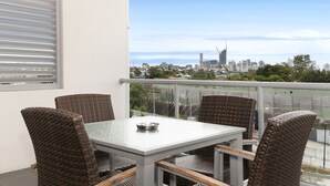 A balcony with a table and chairs, overlooking a cityscape with buildings and greenery. - Hotel Chino (Woolloongabba)