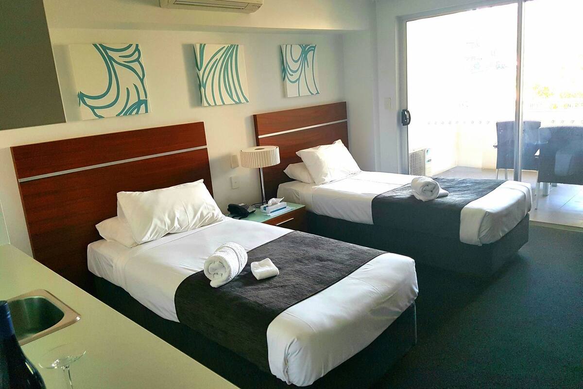 A hotel room with two beds, a desk with a sink, a lamp, and artwork on the wall.