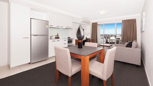 A modern kitchen with white cabinets, a stainless steel refrigerator, and a dining area with a wooden table and chairs. - Hotel Chino (Woolloongabba)