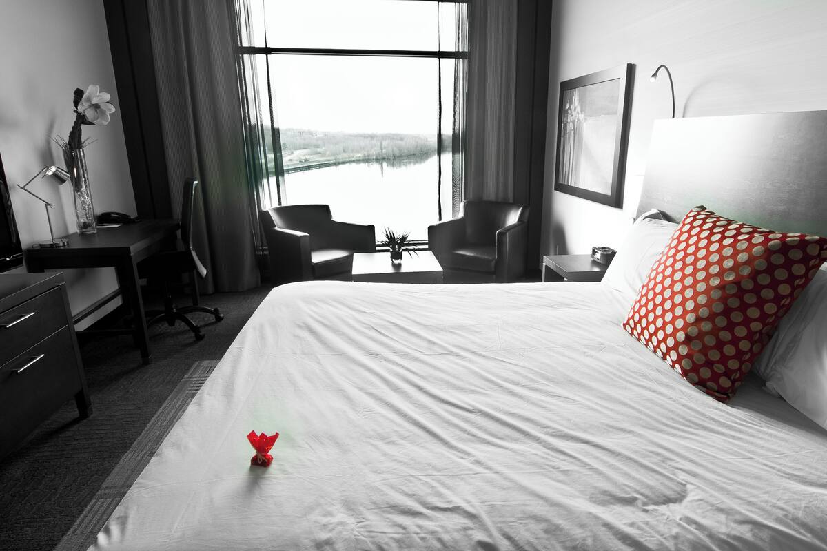 Une chambre d’hôtel avec un lit, un bureau, une chaise, une petite table et une fenêtre donnant sur un paysage agréable.