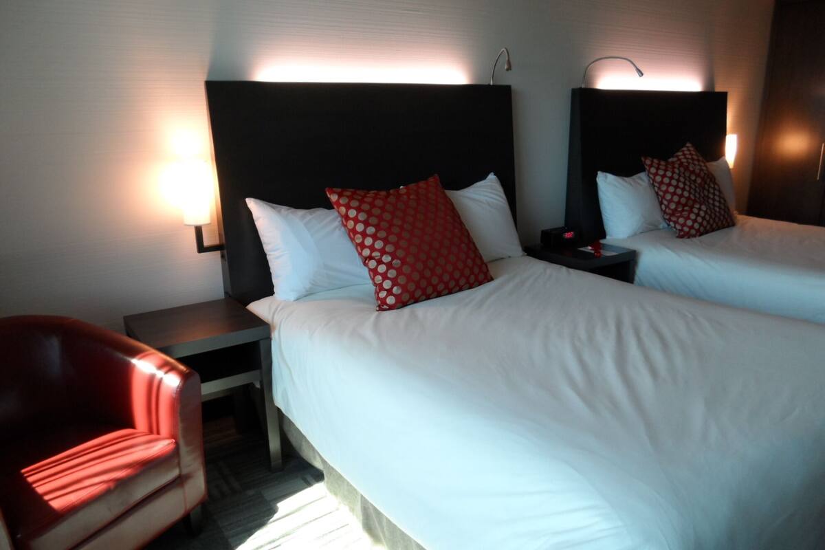 Une chambre d’hôtel avec deux lits, un fauteuil rouge et des tables de chevet.