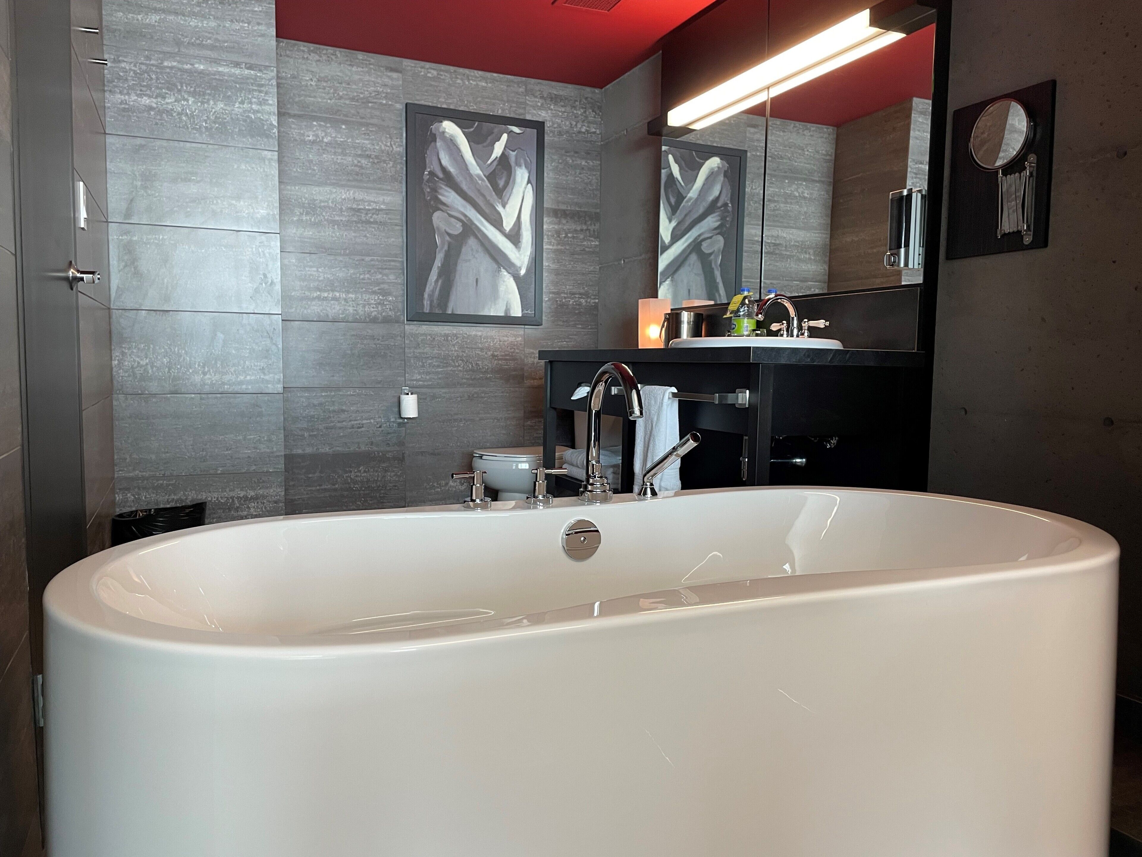 Un baño moderno con una bañera grande, un tocador negro con espejo y un inodoro de pared.