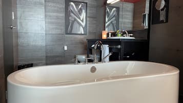 Un baño moderno con una bañera grande, un tocador negro con espejo y un inodoro de pared.