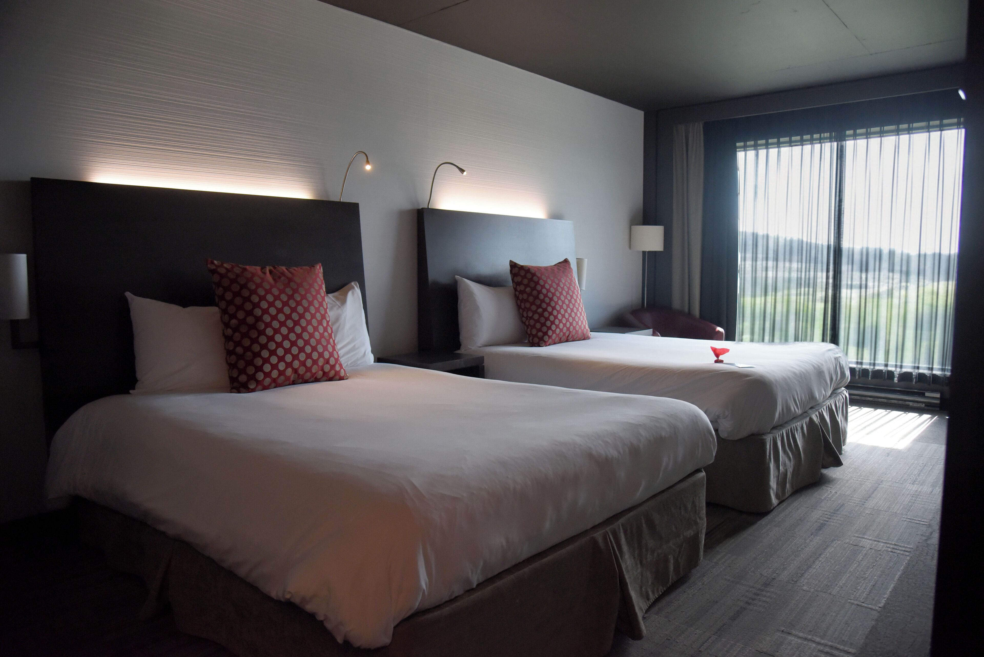 A hotel room with two beds, each with a headboard, a bedside table, and a lamp.