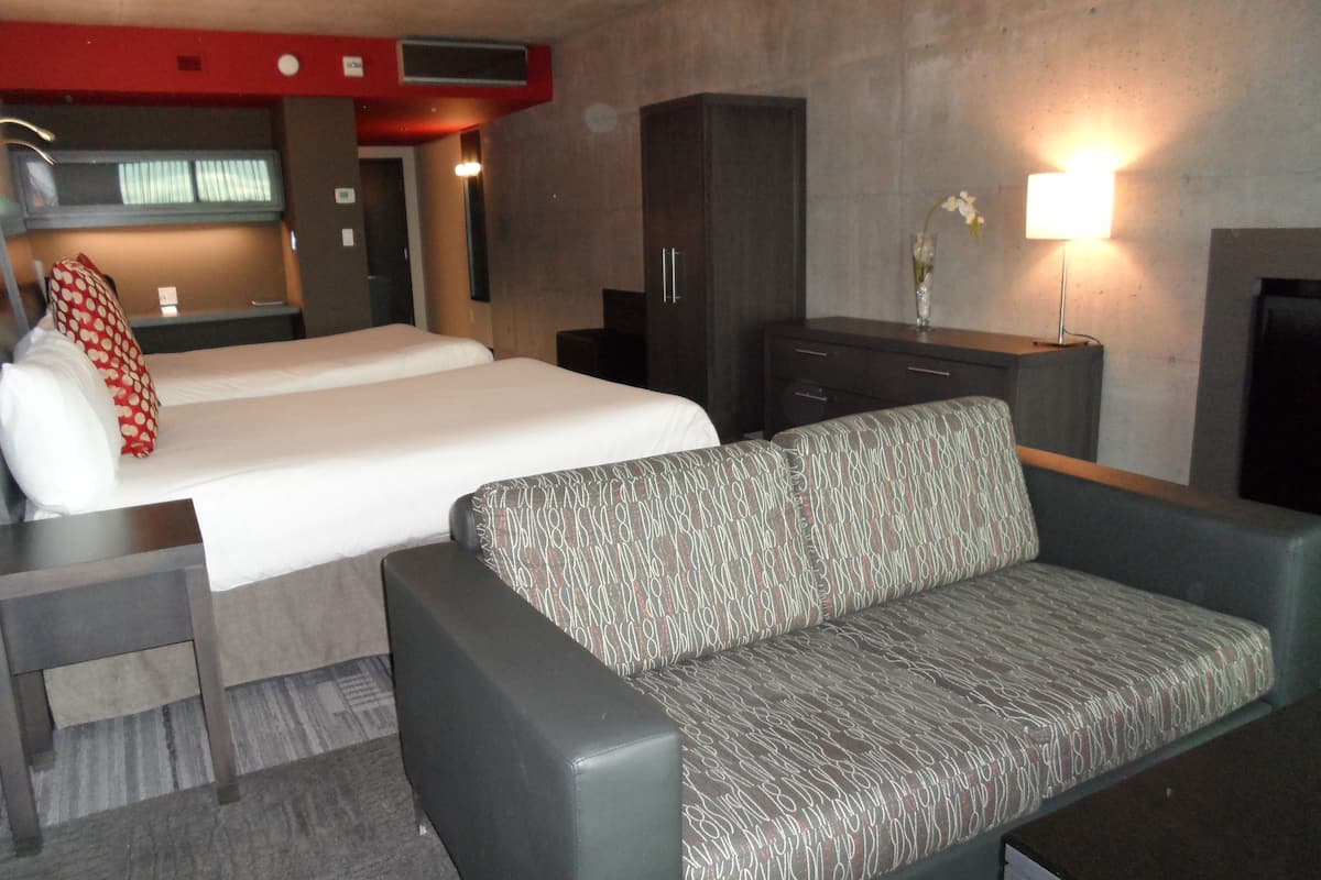 Une chambre d’hôtel avec deux lits, un canapé, un bureau, une armoire et une lampe.