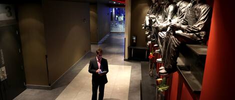A man in a suit standing in a hallway with a statue of soldiers on the right.