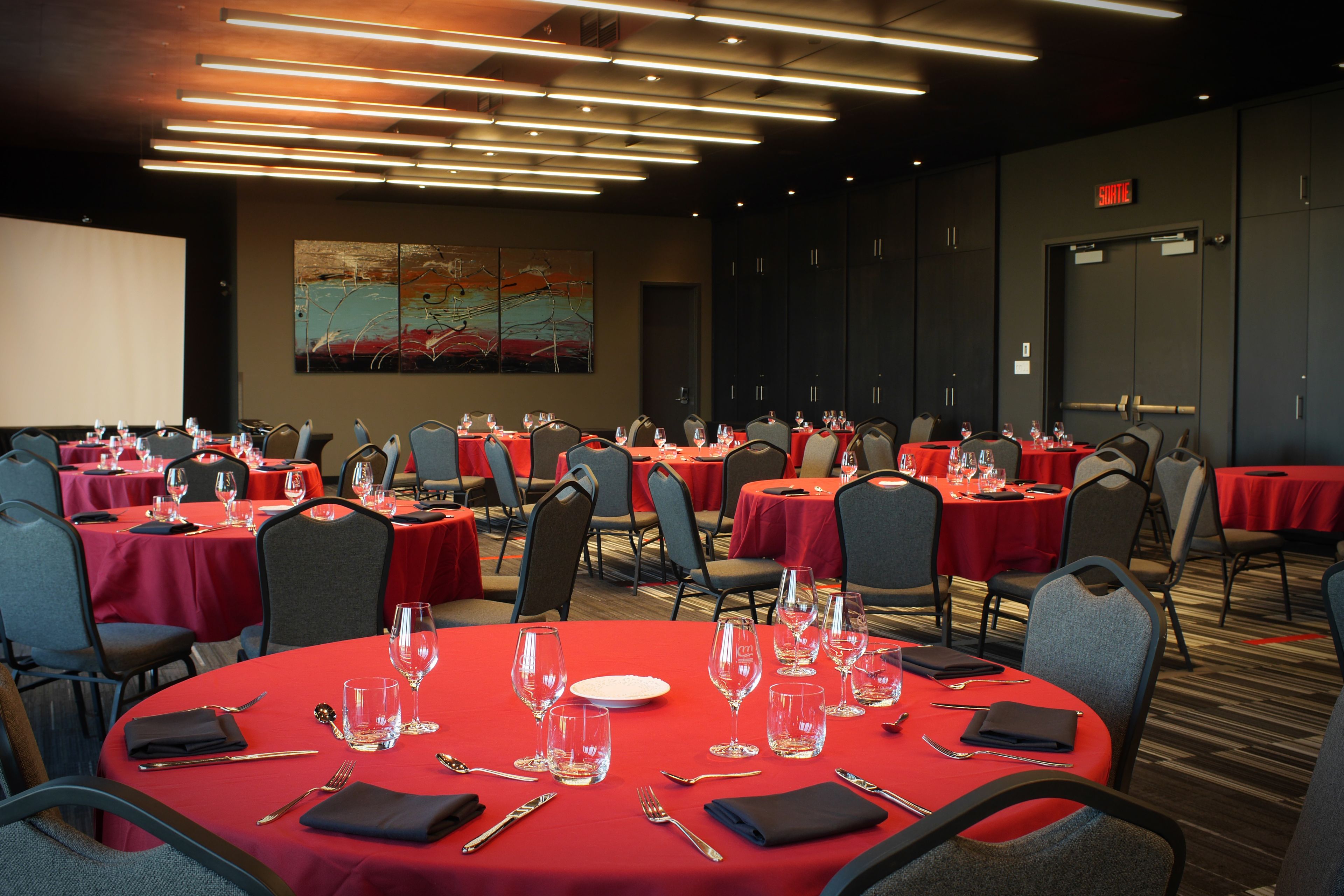 Une salle de conférence dotée de plusieurs tables préparées pour les repas, de chaises et d’un grand écran pour les présentations.