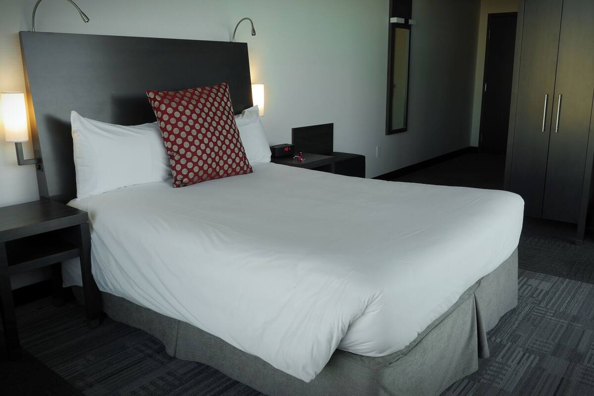Une chambre d’hôtel avec un grand lit, une table de chevet avec une lampe, une armoire et un miroir.