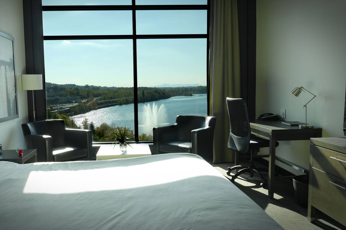 Une chambre d’hôtel avec un grand lit, deux fauteuils, un bureau et une vue sur une rivière.