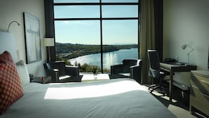 A hotel room with a large bed, two chairs, a desk, and a view of a river.