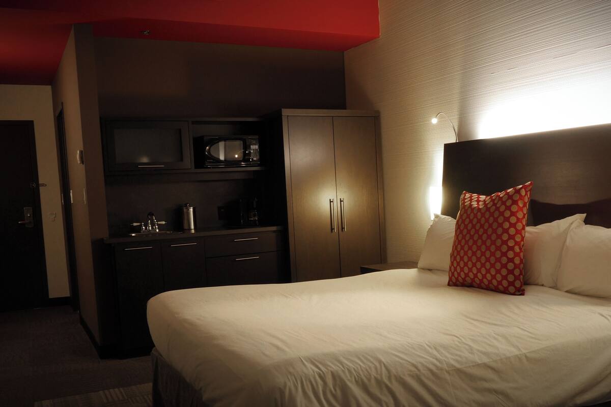 Une chambre d’hôtel avec un lit, une table de chevet, un oreiller rouge, une armoire et un four à micro-ondes.