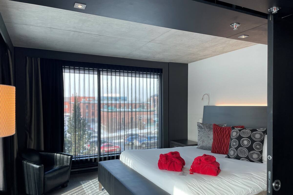 Une chambre d’hôtel moderne, dotée d’un grand lit, d’un bureau et offrant une vue sur le paysage urbain.
