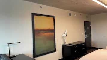 A hotel room with a large painting, a desk, a dresser, and a bed.