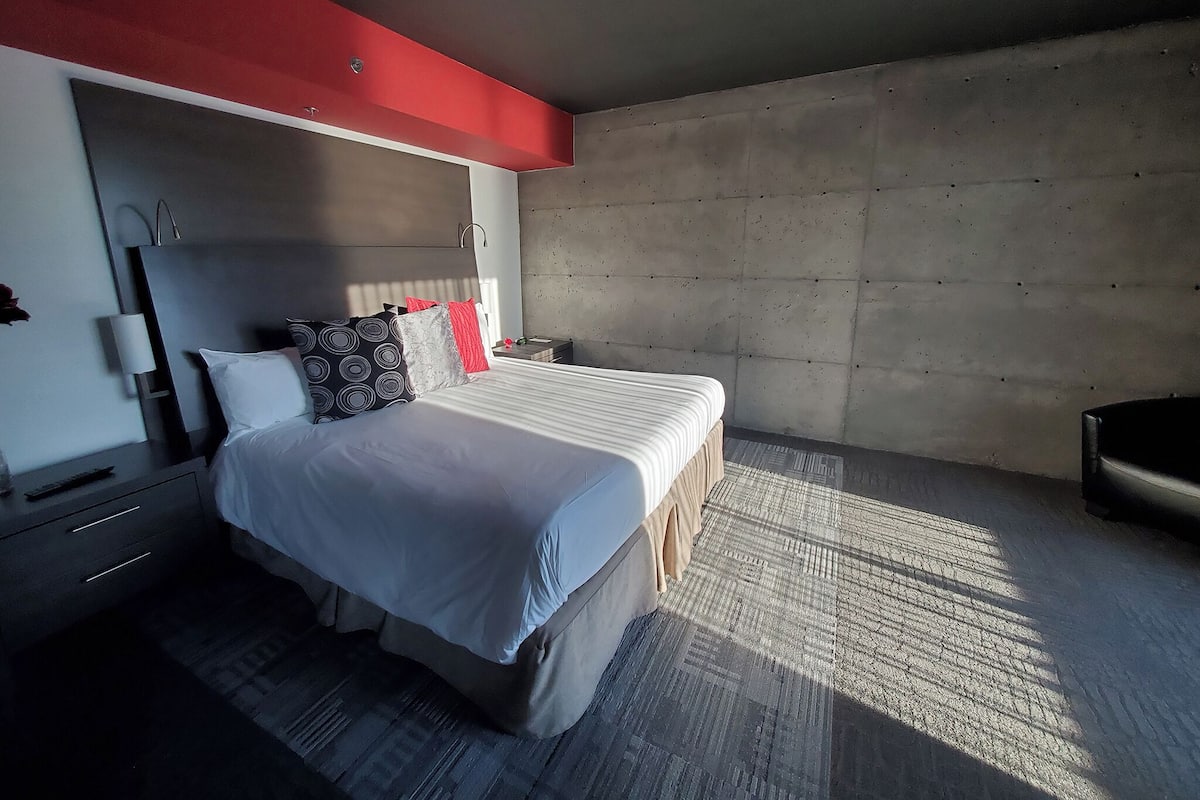 Une chambre d’hôtel moderne avec un grand lit, une table de chevet, un miroir et un mur d’accent de couleur rouge.