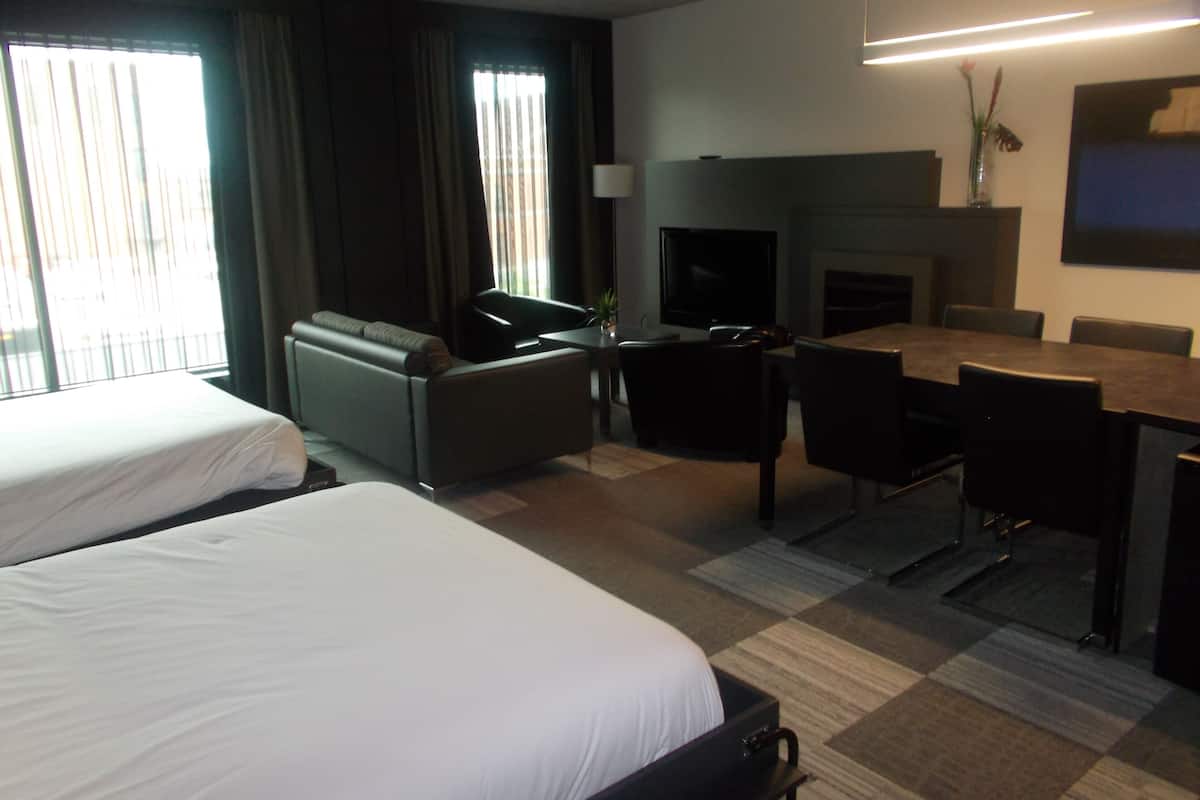 Une chambre d’hôtel avec deux lits, un canapé, une table à manger avec des chaises, une télévision et une cheminée.