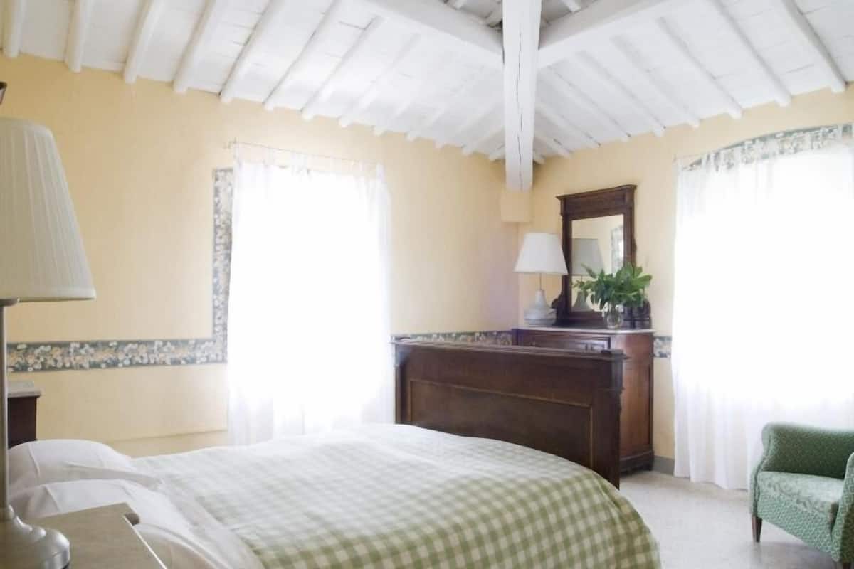 A hotel room with a bed, a desk, a chair, a lamp, a mirror, and a window with curtains.