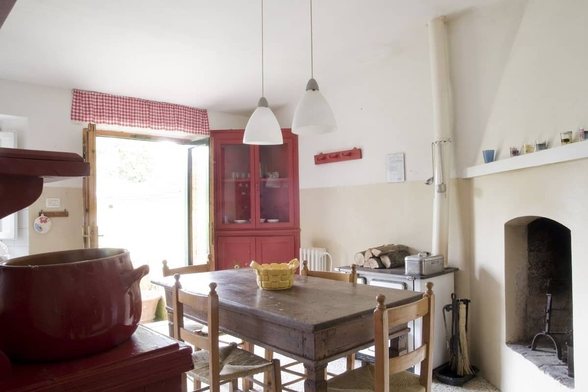 A kitchen with a wooden table, chairs, a red cabinet, and a fireplace.