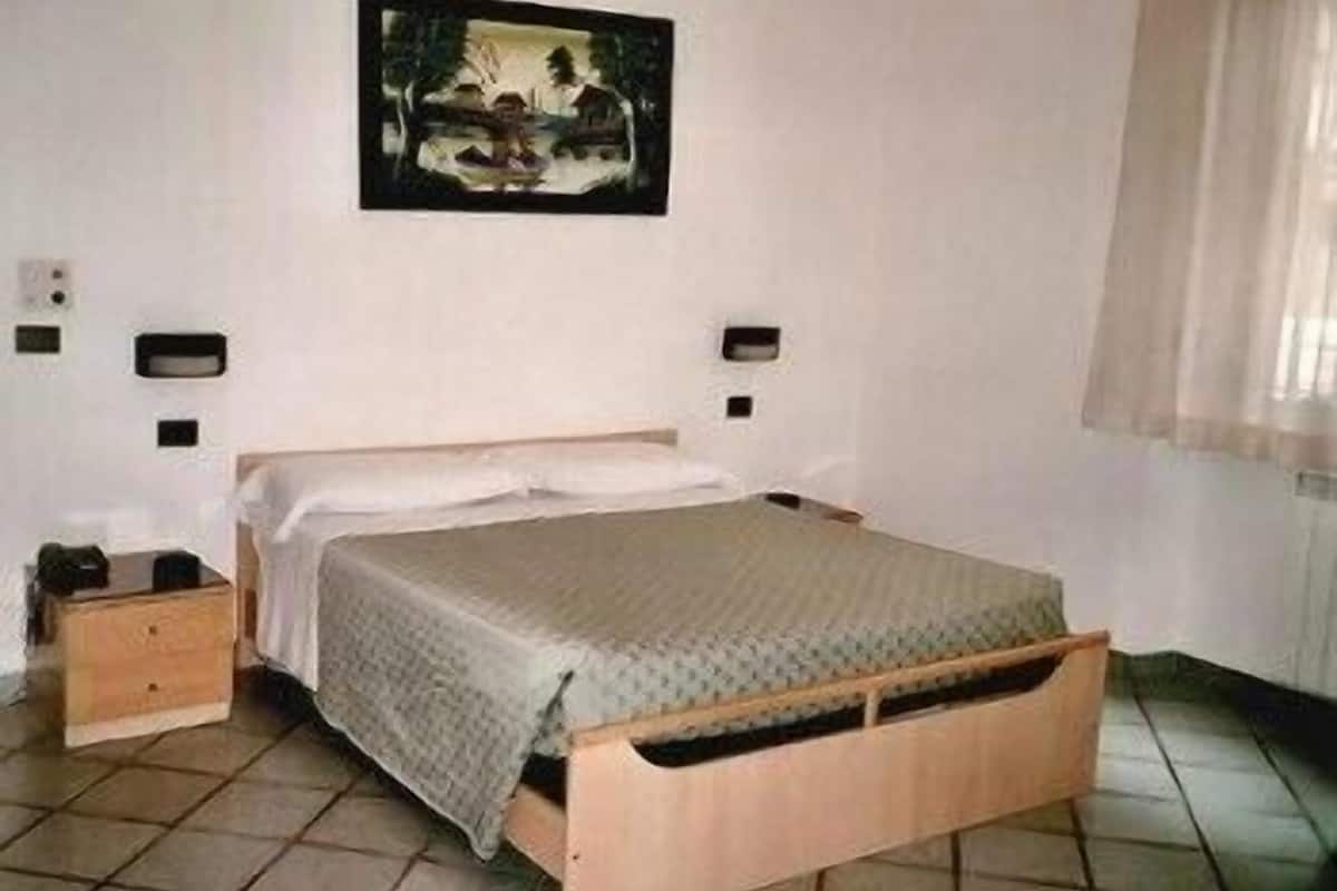 A bedroom with a wooden bed, a nightstand, a wall-mounted light, and a painting above the bed.