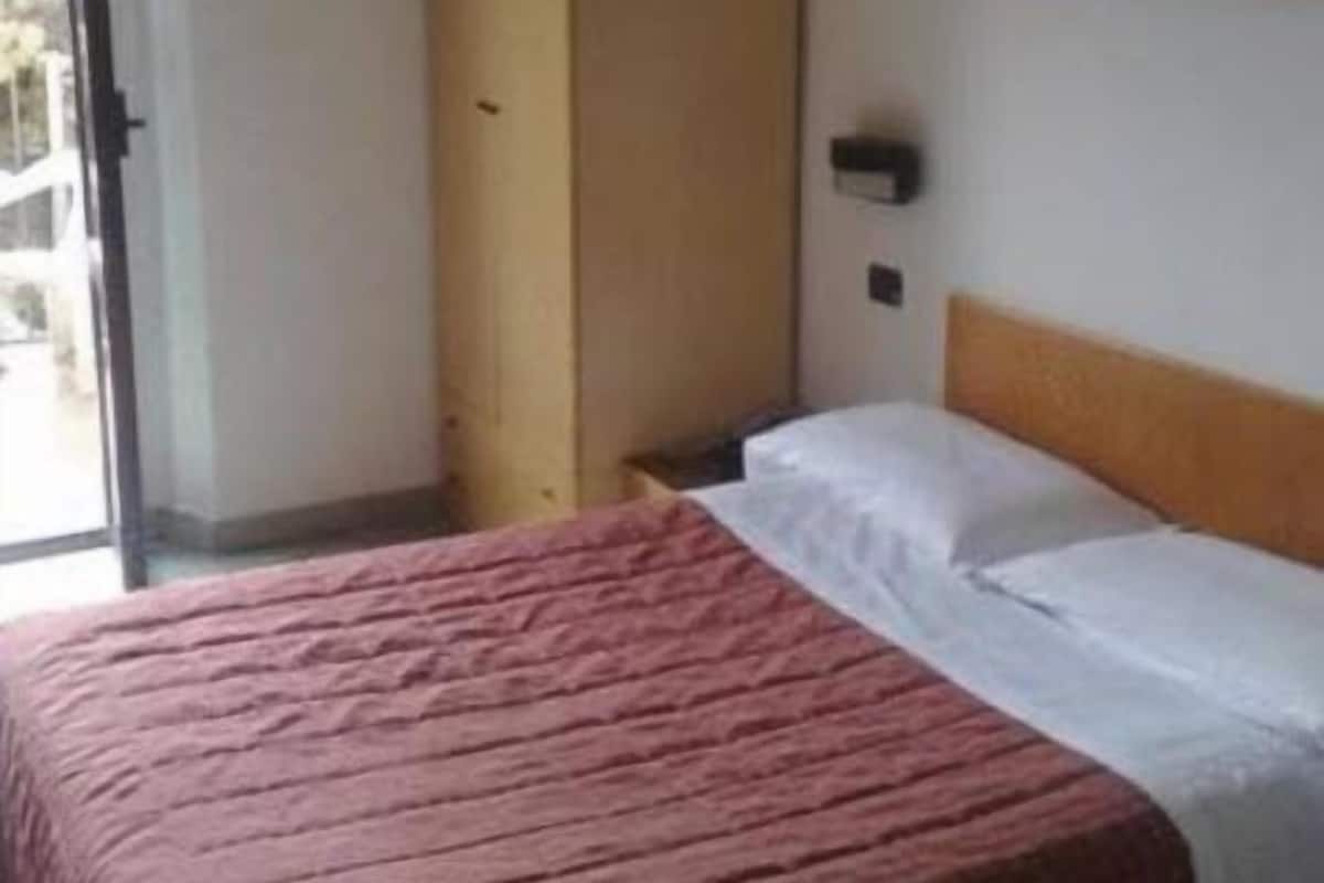A hotel room with a bed, a wardrobe, and a painting on the wall.