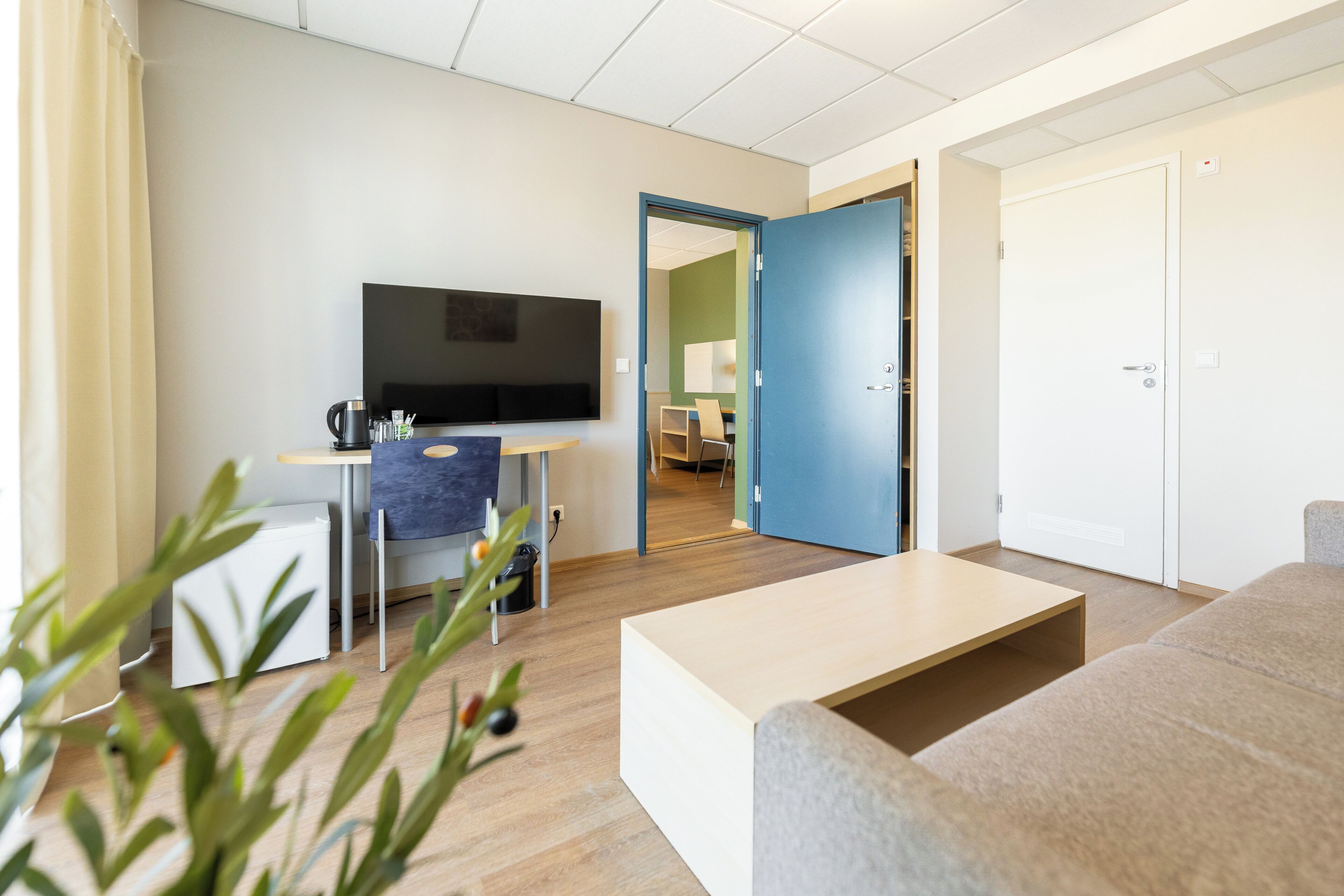 Una sala de estar moderna con un televisor de pantalla plana, una mesa de centro, un sofá y una puerta que da a otra habitación.