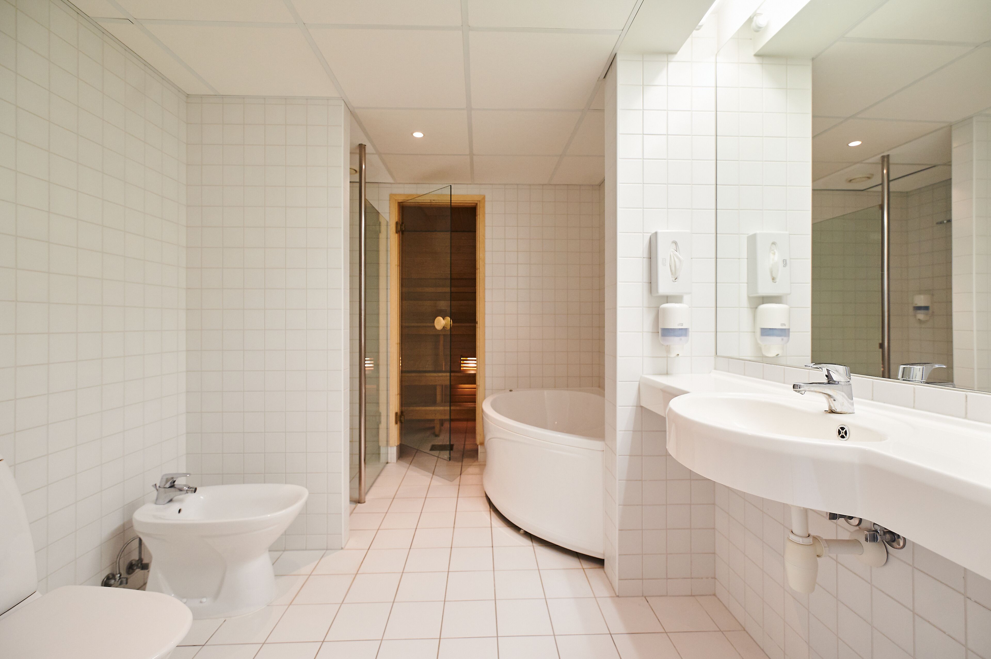 Un baño moderno con bidé, inodoro, bañera y un lavamanos grande con espejo.