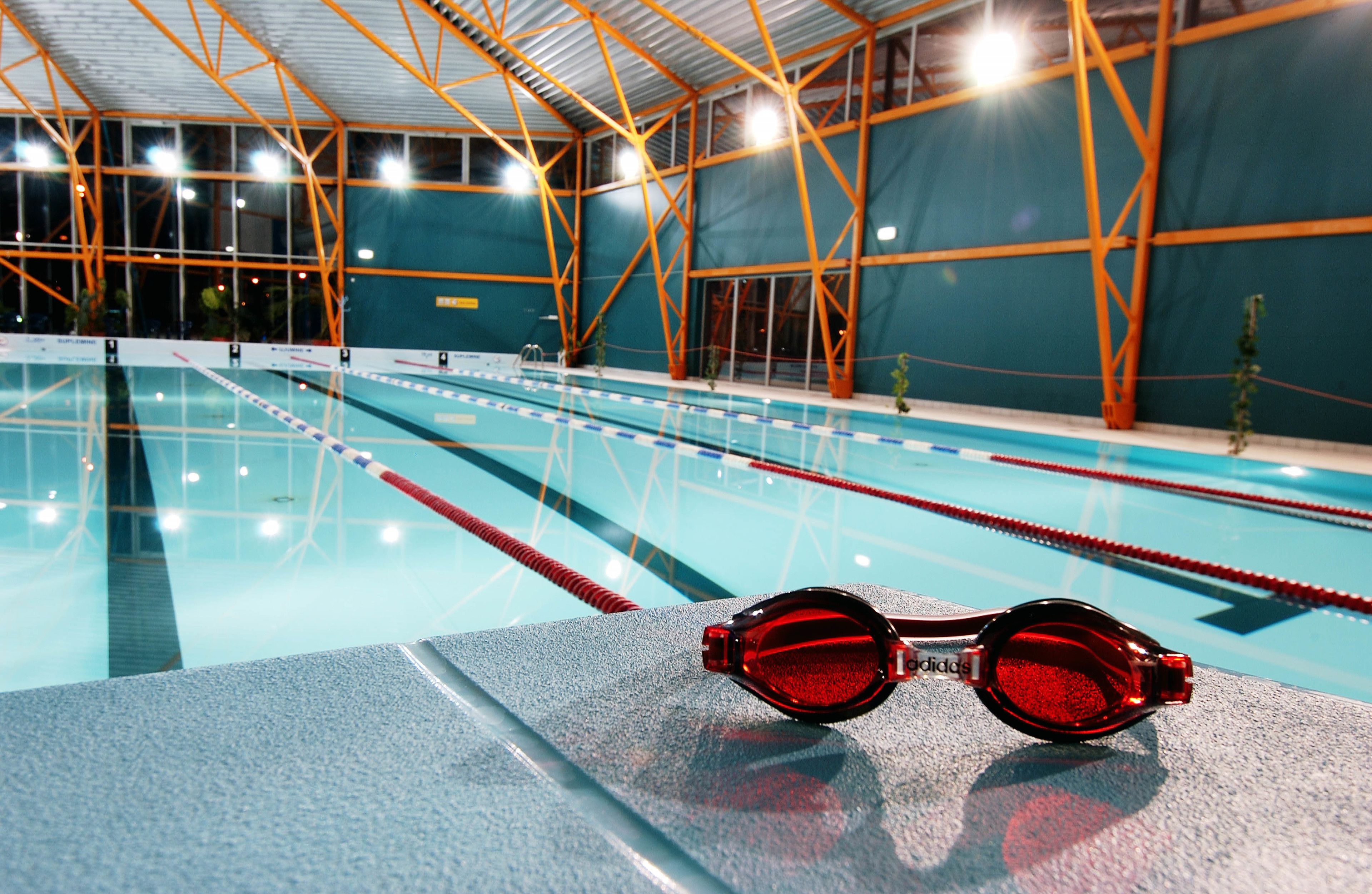 Una piscina interior con carriles de natación, un trampolín y un par de gafas sobre el borde.