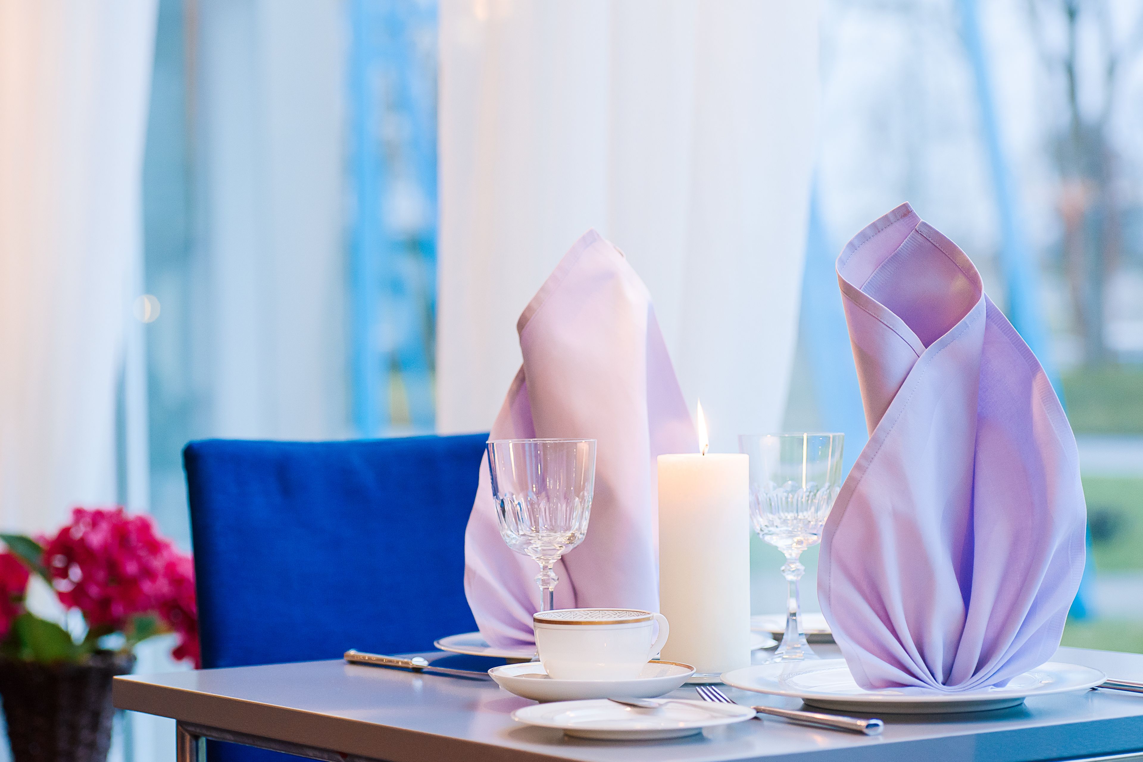 A table set with a white cup, a glass, and a candle, with a blue chair in the background.