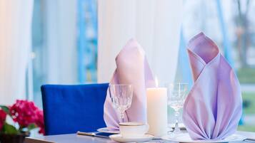 A table set with a white cup, a glass, and a candle, with a blue chair in the background.