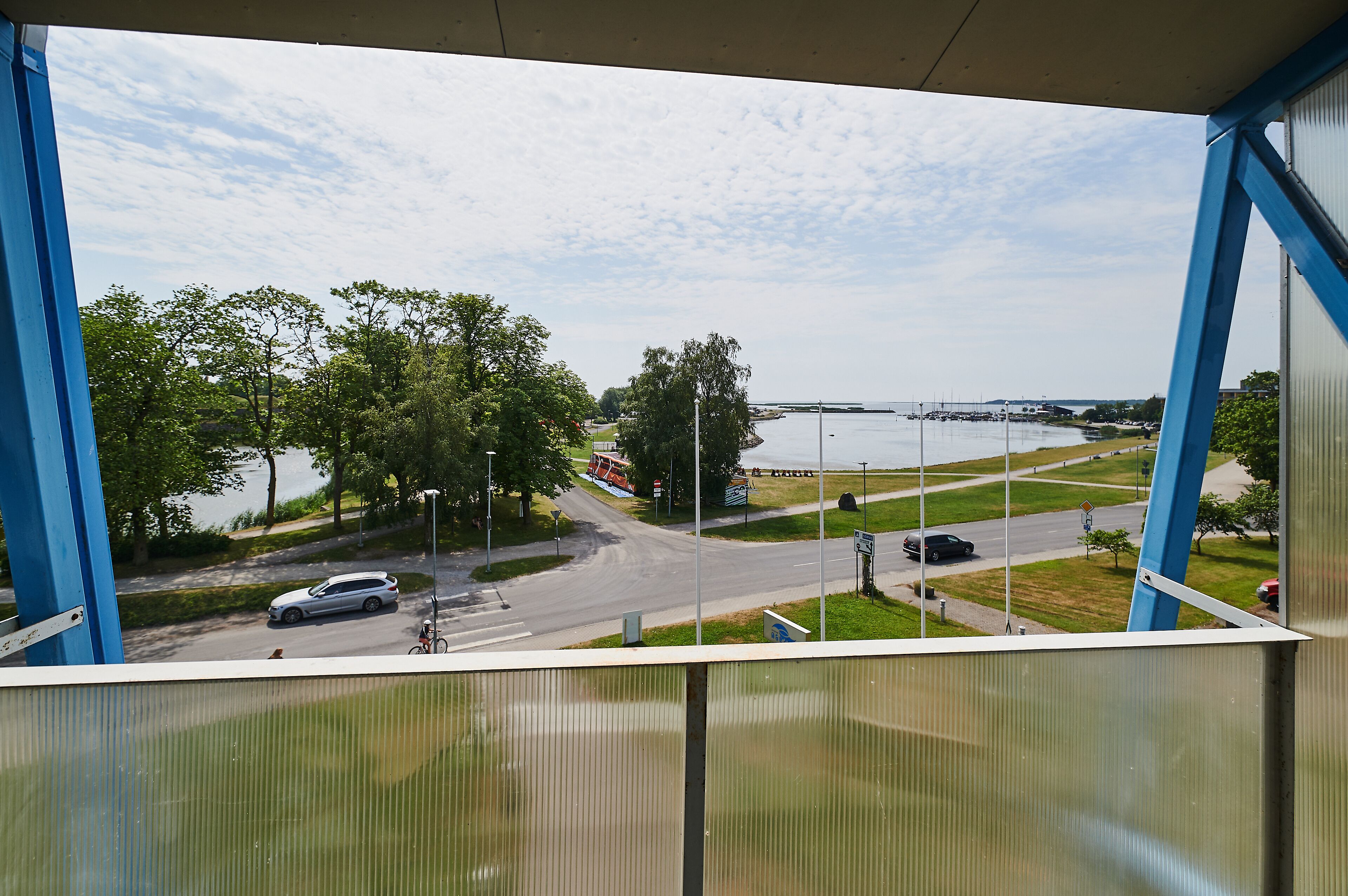 A view from a balcony overlooking a road with a bridge in the distance, trees, and a grassy area.