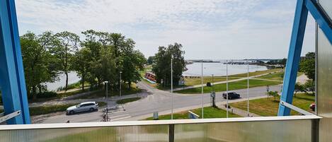 A view from a balcony overlooking a road with a bridge in the distance, trees, and a grassy area.
