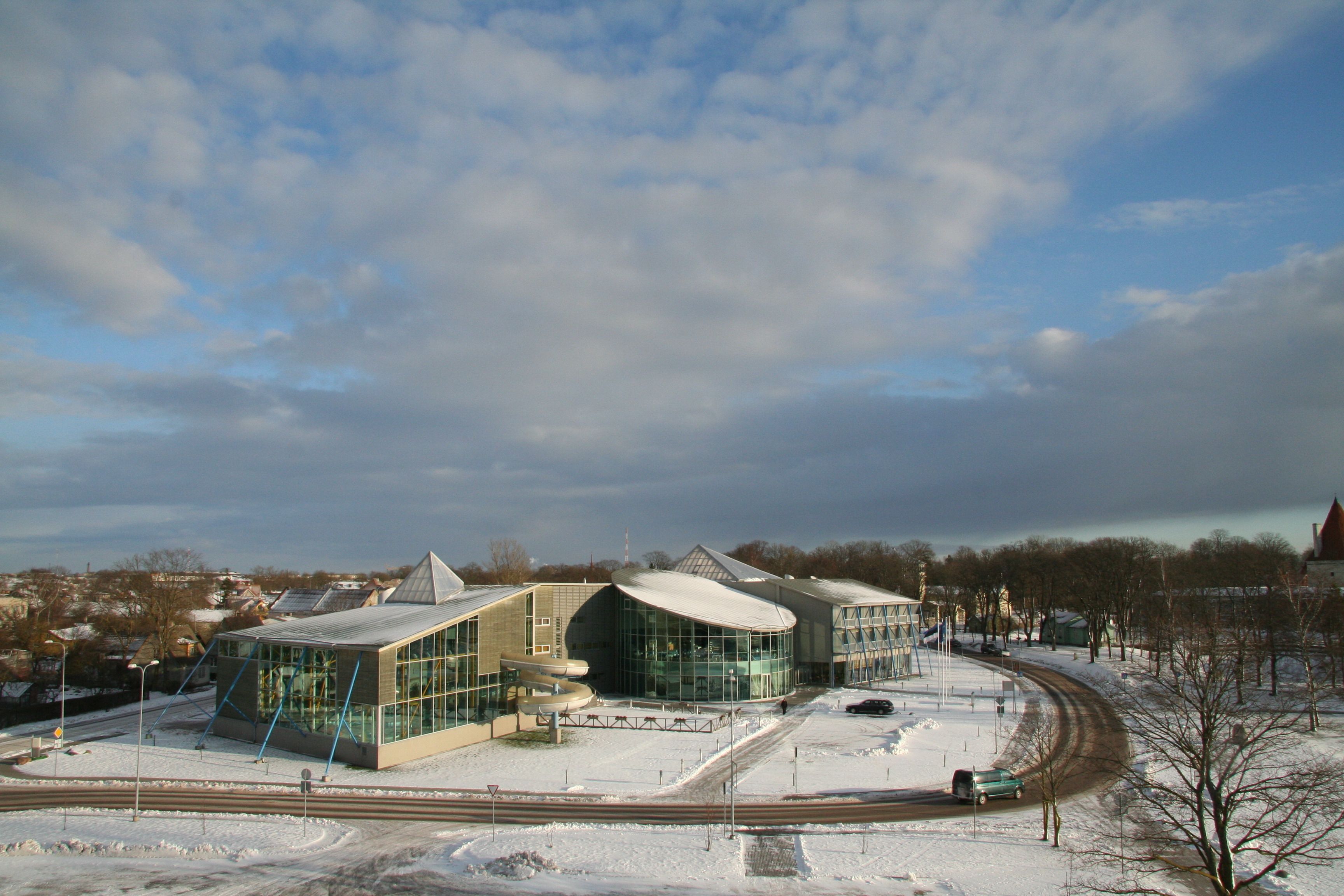 A modern building with large glass windows and a curved roof, surrounded by snow and a railway track.