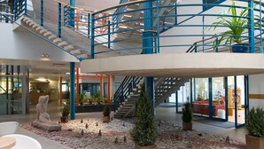 A spacious lobby with a central staircase, seating areas, and potted plants. - Asa Spa Hotel (Kuressaare)