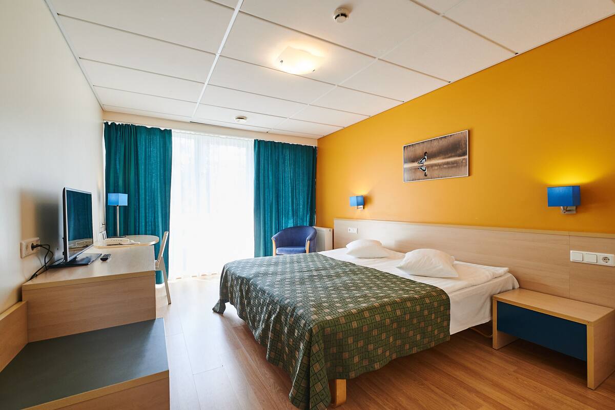 Une chambre d’hôtel comprenant un lit, un bureau avec un ordinateur, une chaise et une table de chevet.