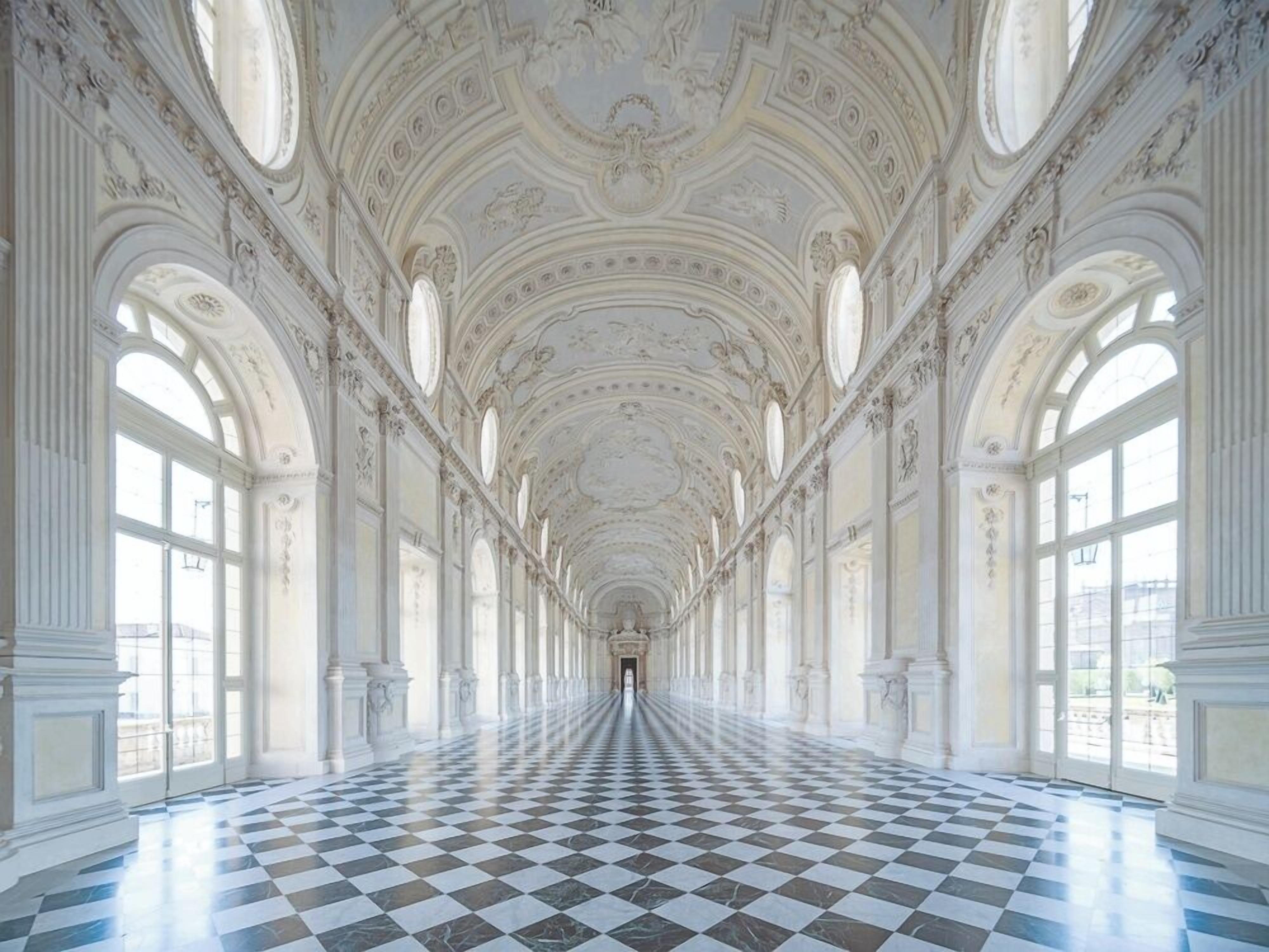 A long corridor with a checkered floor, arched windows, and ornate ceiling decorations.