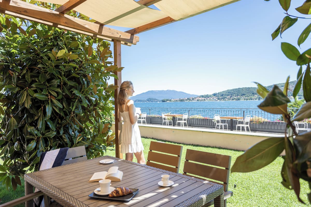 Une terrasse avec une table dressée pour deux personnes, offrant une vue sur un plan d’eau et des collines.