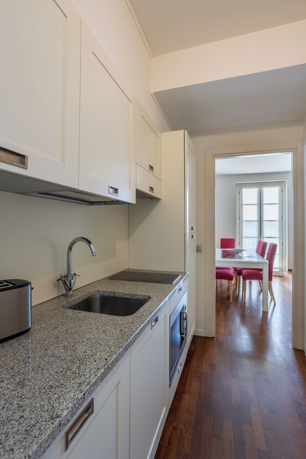 A modern kitchen with white cabinets, granite countertops, a stainless steel sink, and a toaster. - Resort Antico Verbano (Meina)